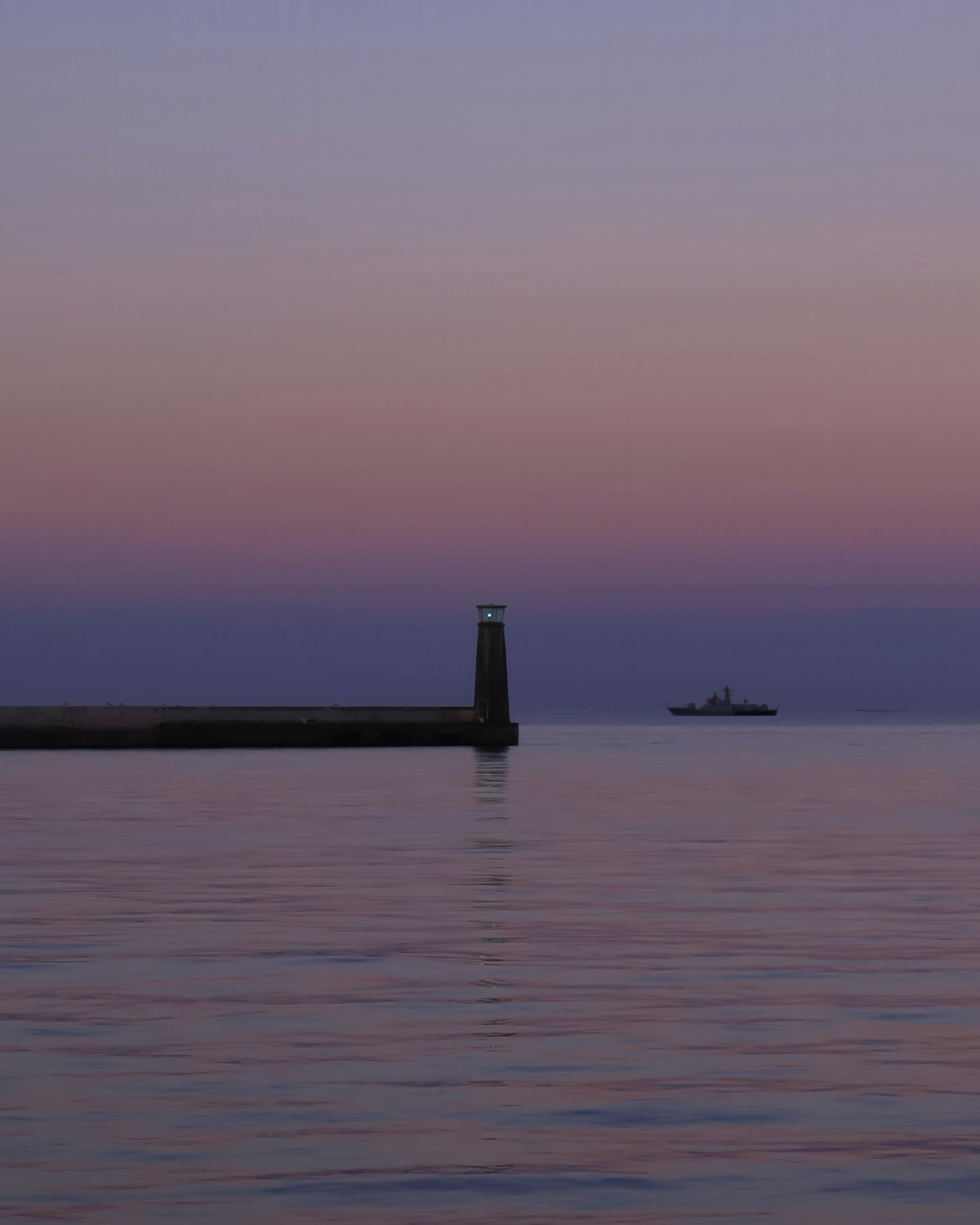 Lighthouse on pier at sunset in Gdynia, Poland, with a large ship at sea in the background