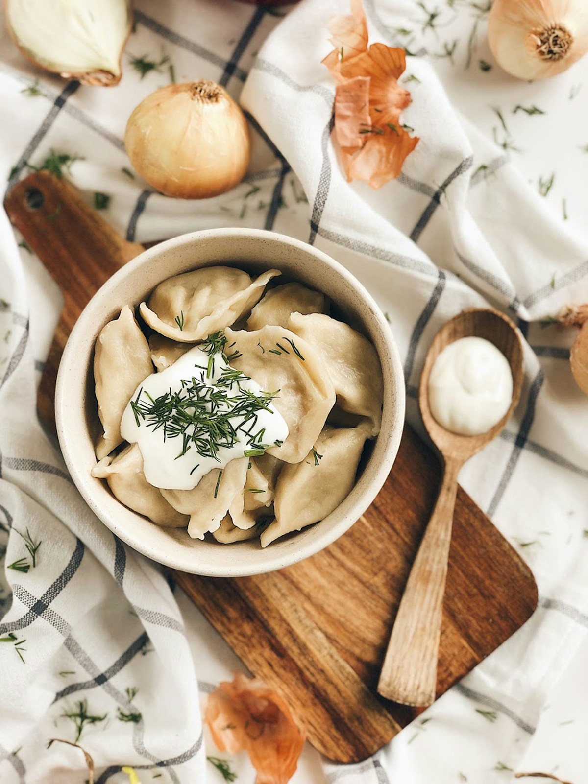 Bowl of pierogi dumplings with sour cream and fresh dill garnish on a wooden board