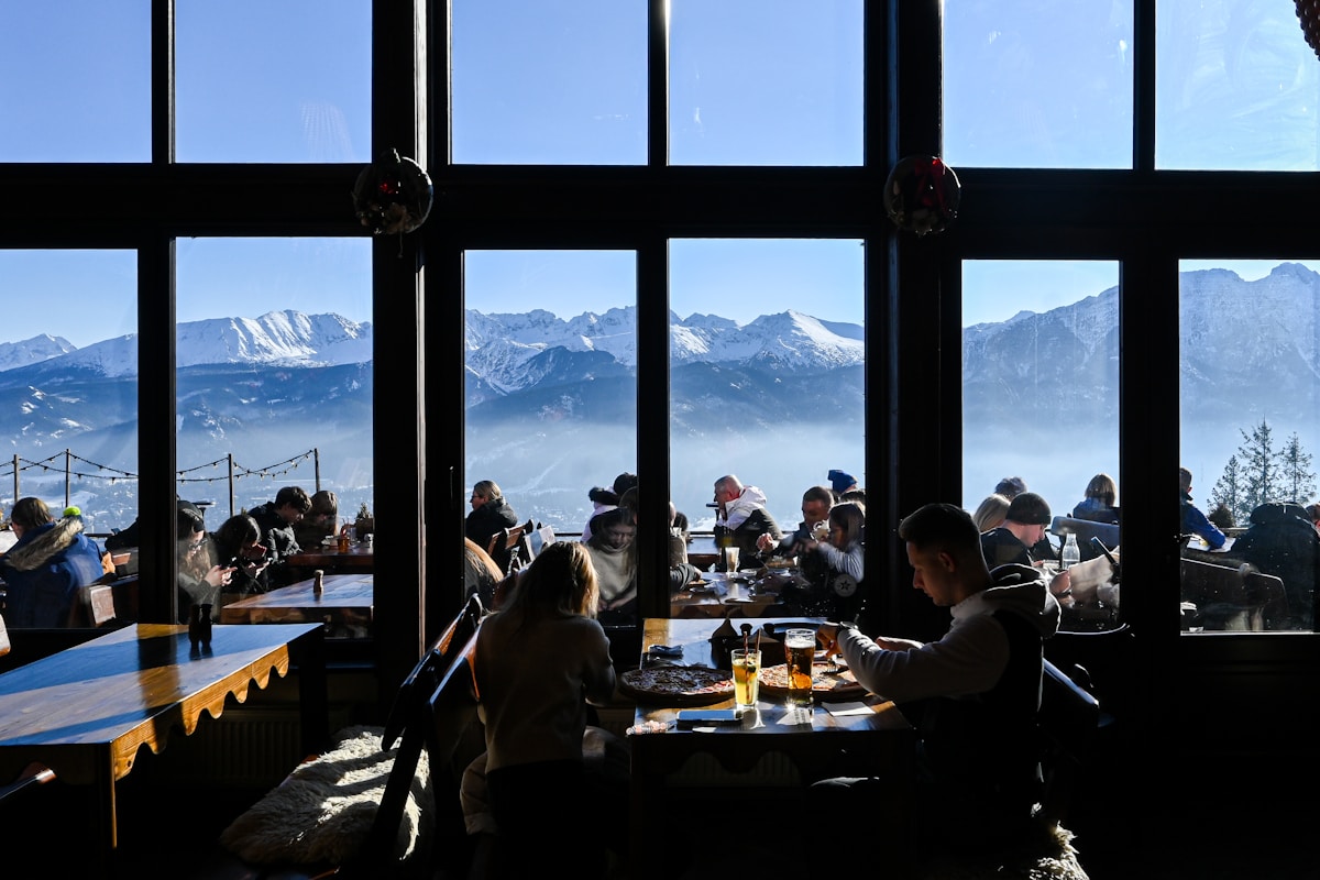 Mountain restaurant interior with diners and panoramic snowy Tatra peak views through large windows, Zakopane, Poland