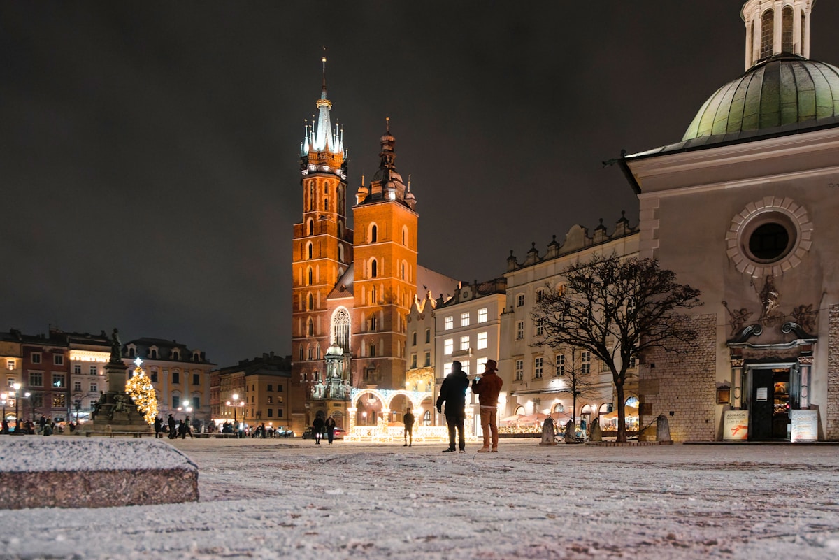 Kraków's Main Market Square at night with St Mary's Basilica illuminated and snow on the ground, Poland
