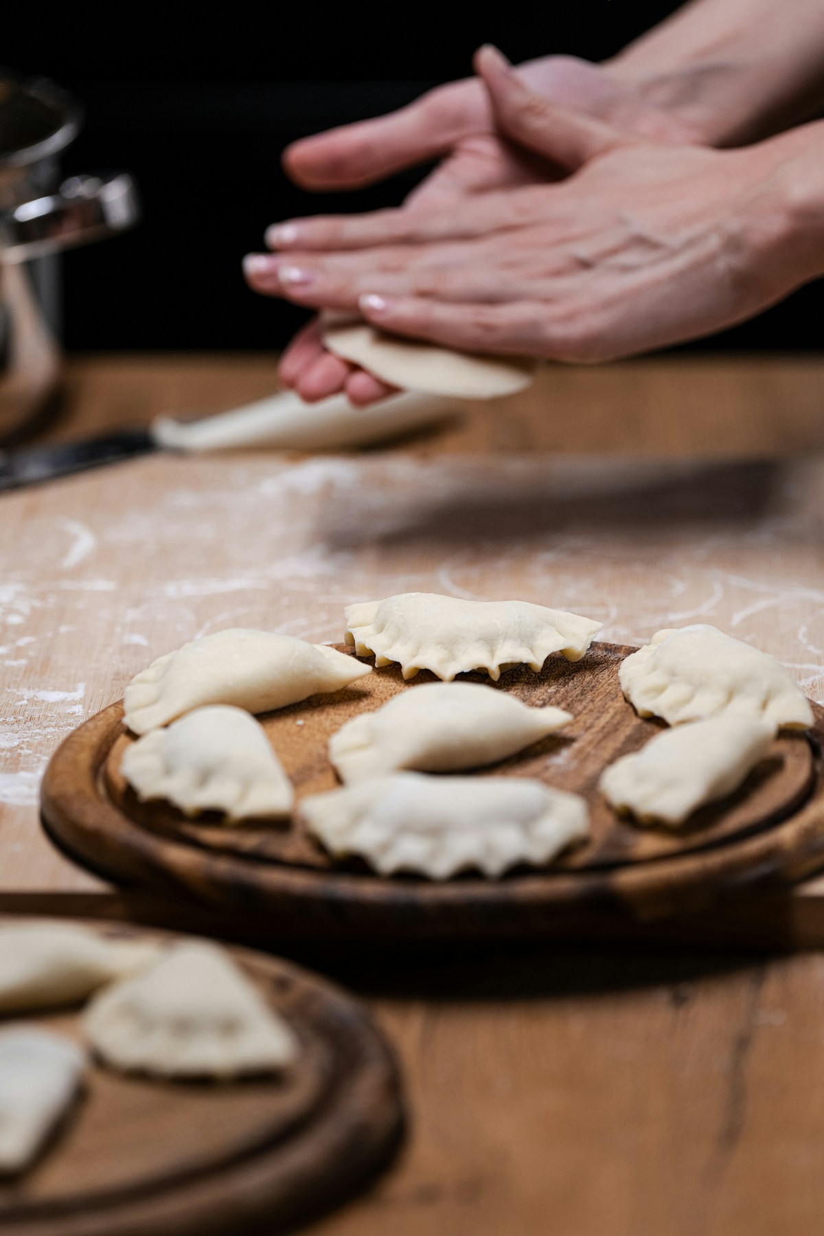 Hands shaping raw pierogi dumplings on a floured wooden board — traditional Polish food preparation
