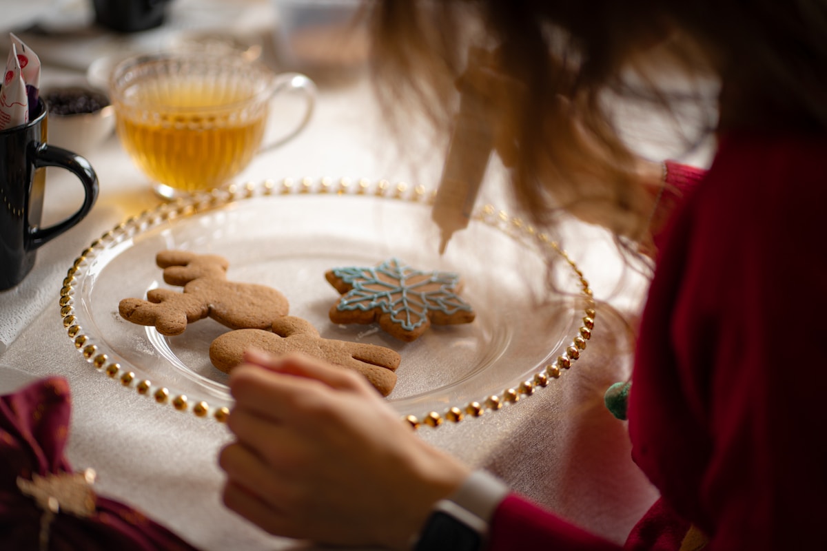 Handmade gingerbread cookies in reindeer and snowflake shapes being decorated with icing on a white plate, Toruń piernik tradition