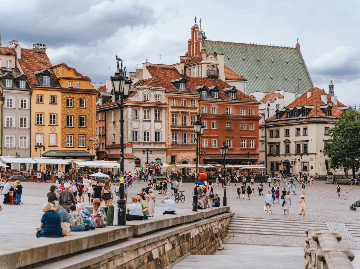 Warsaw Old Town Square in summer with colourful historic buildings and people sitting on steps, Poland