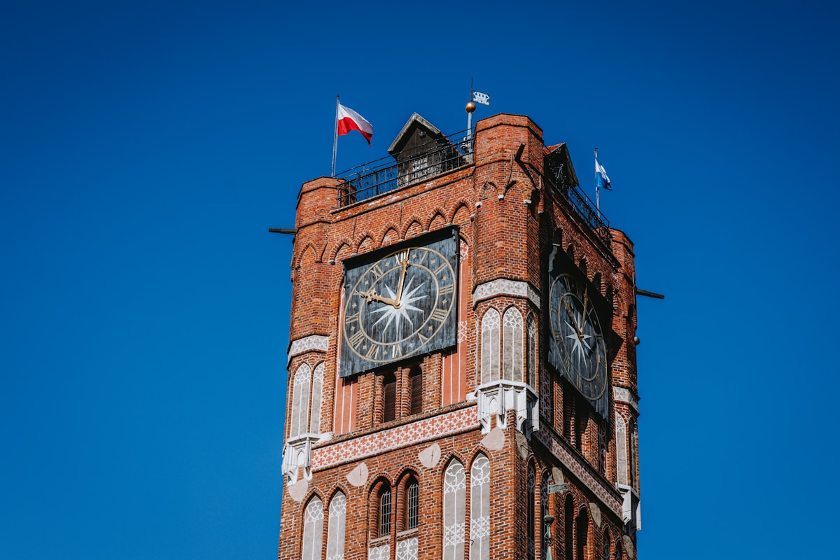 Gothic brick Town Hall clock tower with Polish flag against blue sky in Toruń, Poland