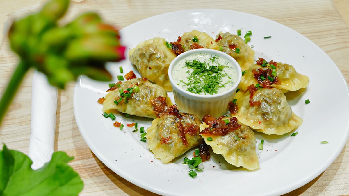 Plate of Polish pierogi dumplings with sour cream dip, garnished with chives and crispy onion