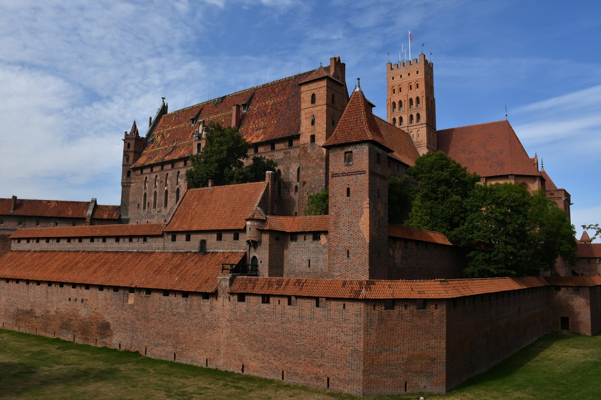 Malbork Castle red brick fortress walls and towers under blue sky, Poland