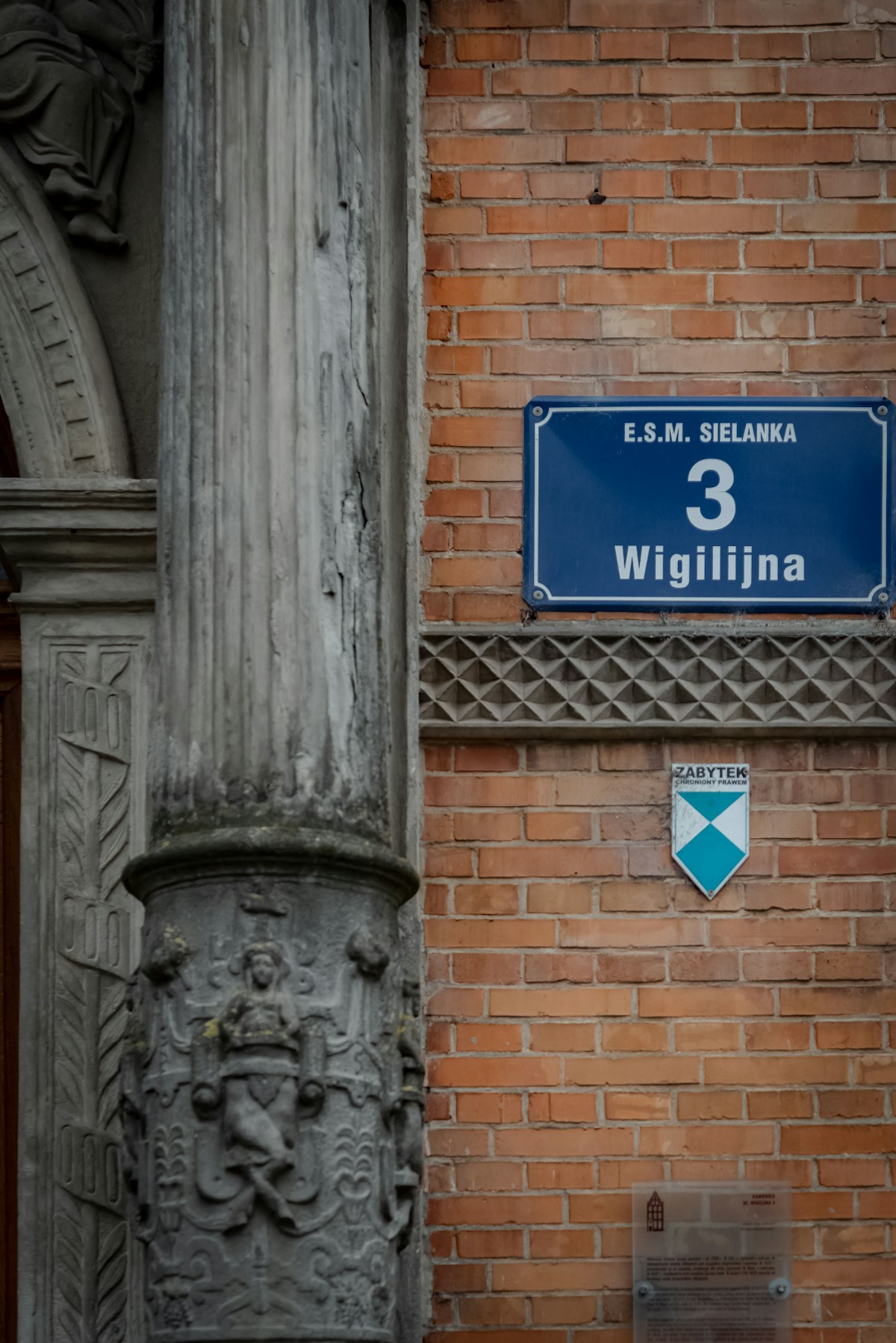 Blue street sign with Polish text on a brick building in Elbląg, Poland