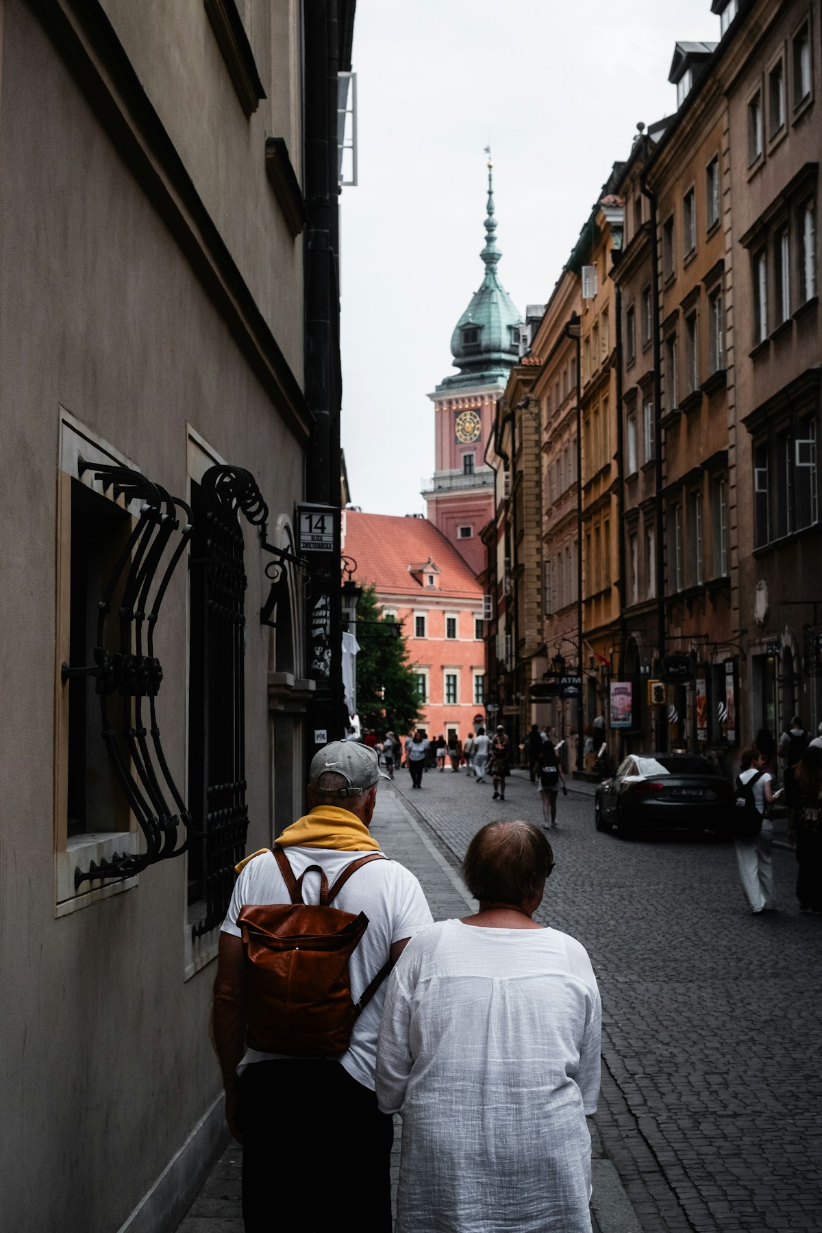 Tourists walking down a cobblestone street in Warsaw Old Town with the Royal Castle in the background, Poland