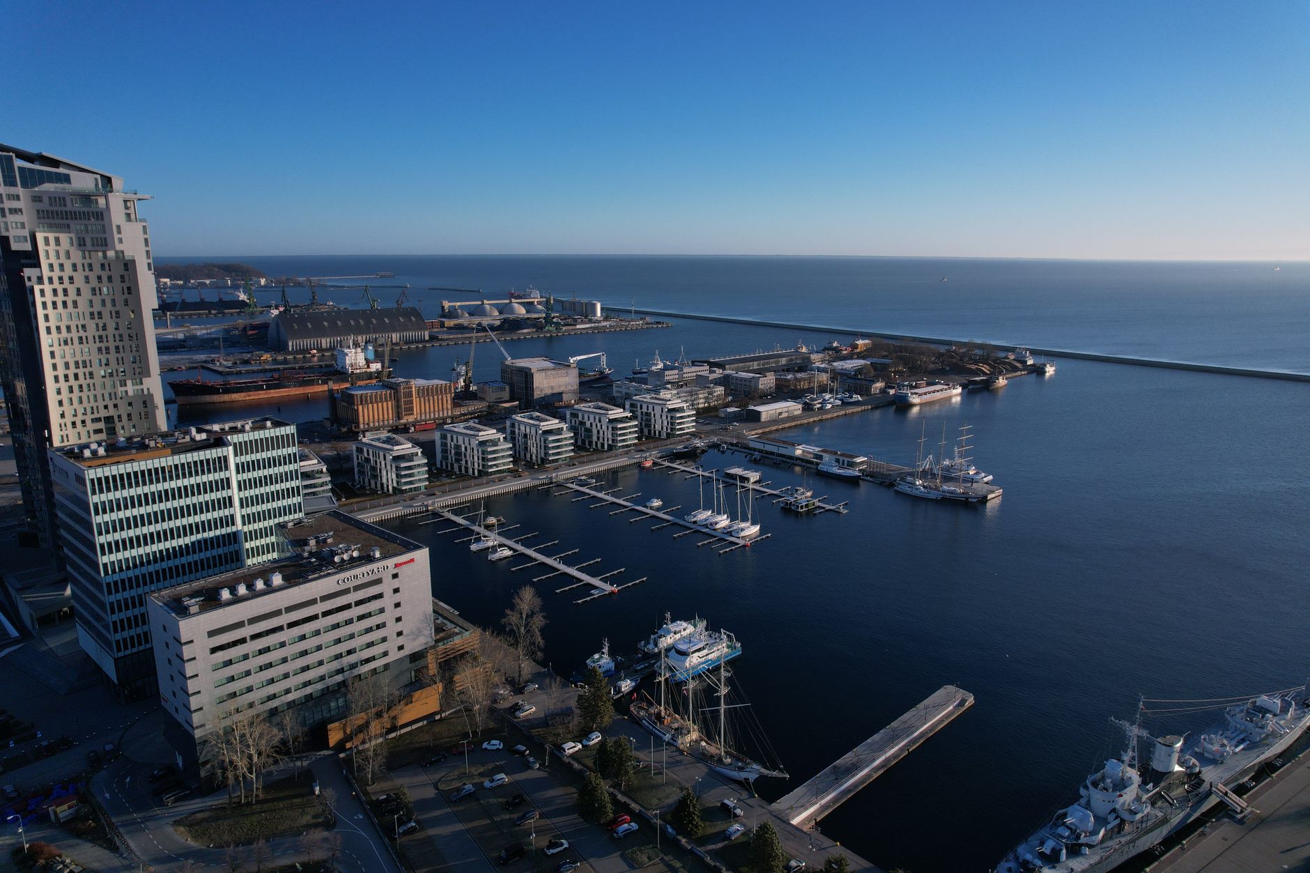 Aerial view of Gdynia harbour with marina, yachts and modern waterfront buildings under a blue sky, Poland